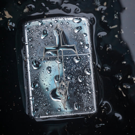 Metallic lighter with a cross design on a dark surface with water droplets.